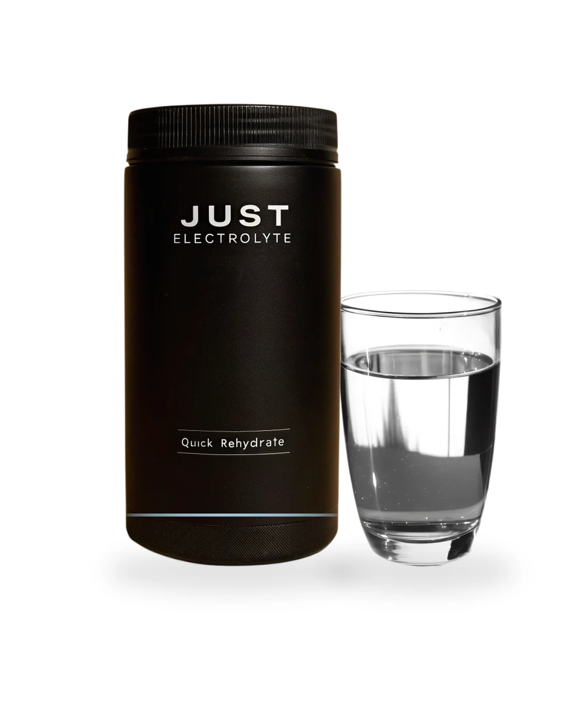 Matte-black Just Electrolyte Quick Rehydrate tub beside a clear glass of prepared electrolyte water, soft studio shadow on a white background